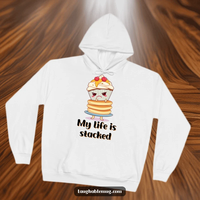 Funny hoodie depicting a grumpy cupcake attempting to balance a huge, unstable stack of pancakes, radiating relatable frustration.