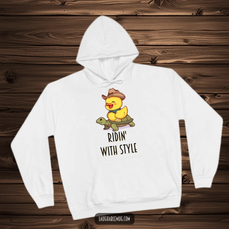 Funny hoodie featuring a giggling duck cowboy attempting to ride a turtle, offering warmth and humor.